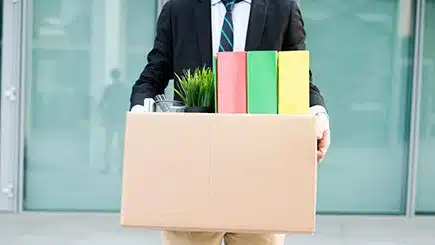 Man in suit carrying box of books papers and vase.